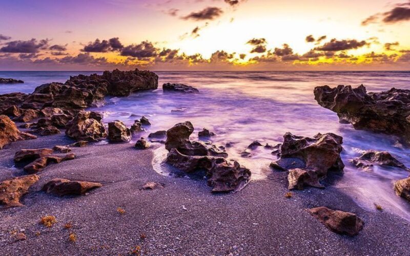 Surf washing between jagged shoreline rocks beneath a warm, cloud-filled sky
