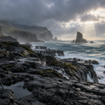 Wooden tripod overlooking a storm-lit rocky coastline and sea stacks after rain.