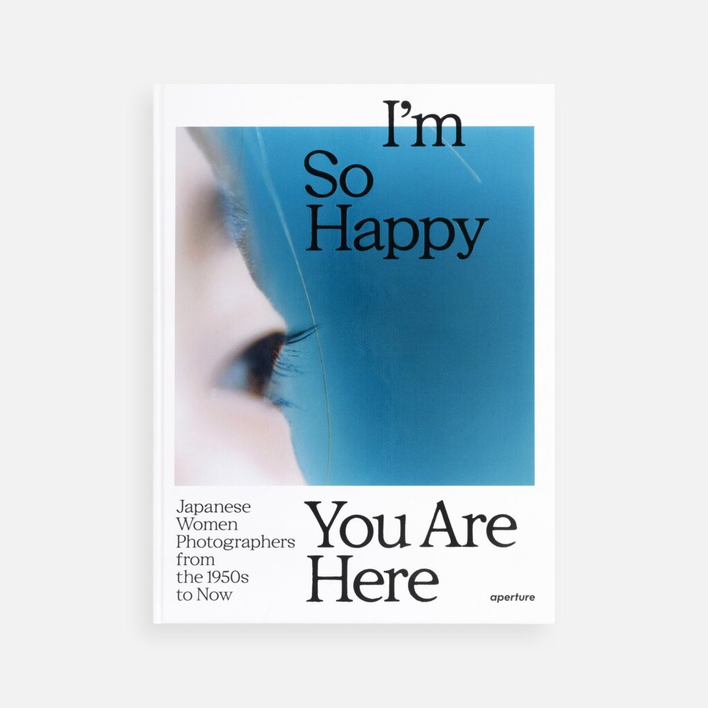 Aperture’s I’m So Happy You Are Here book cover, with black lettering over a blue photographic detail.