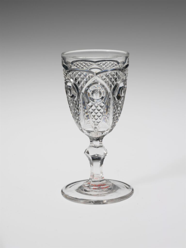 Historic stemmed wine glass photographed against a plain background.