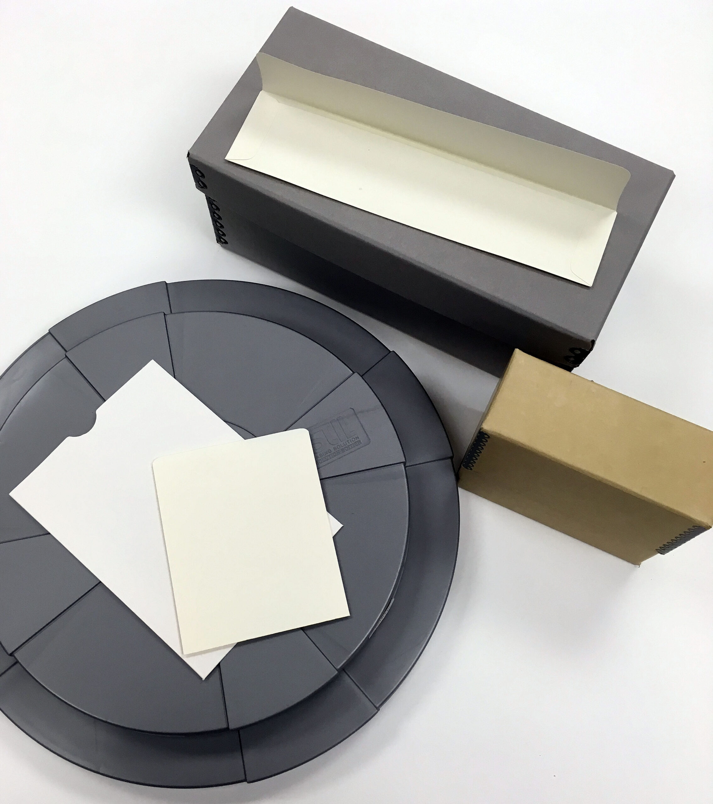 Photographic preservation enclosures, paper sleeves and archival boxes arranged on a white surface.