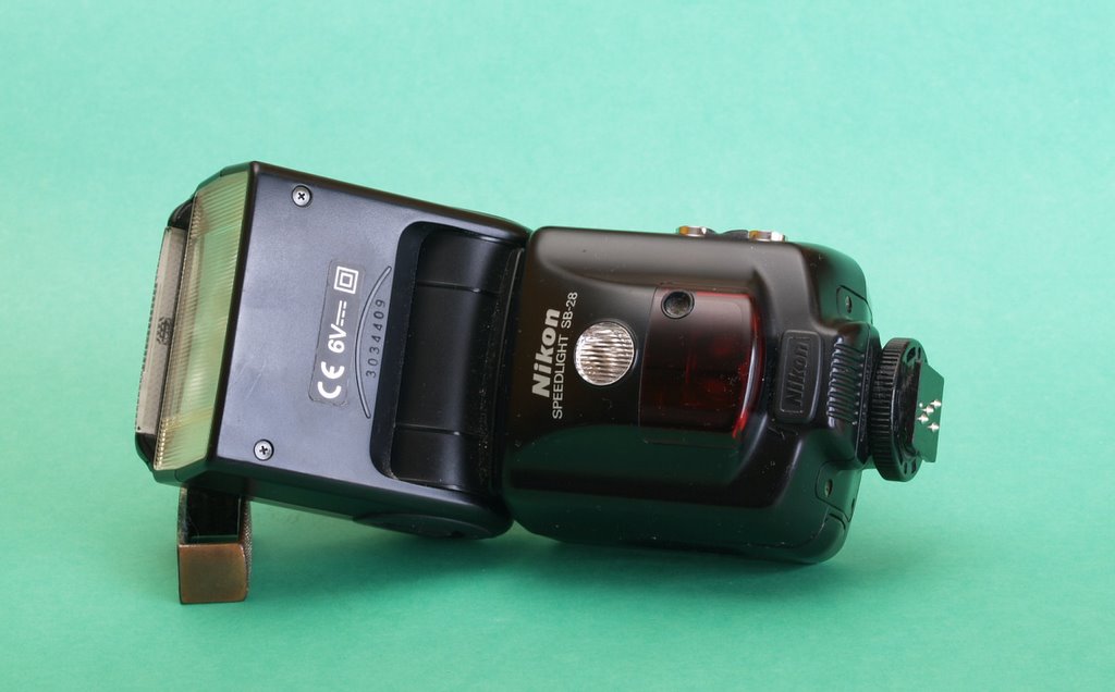A black Nikon Speedlight SB-28 flash unit resting on a solid green background.